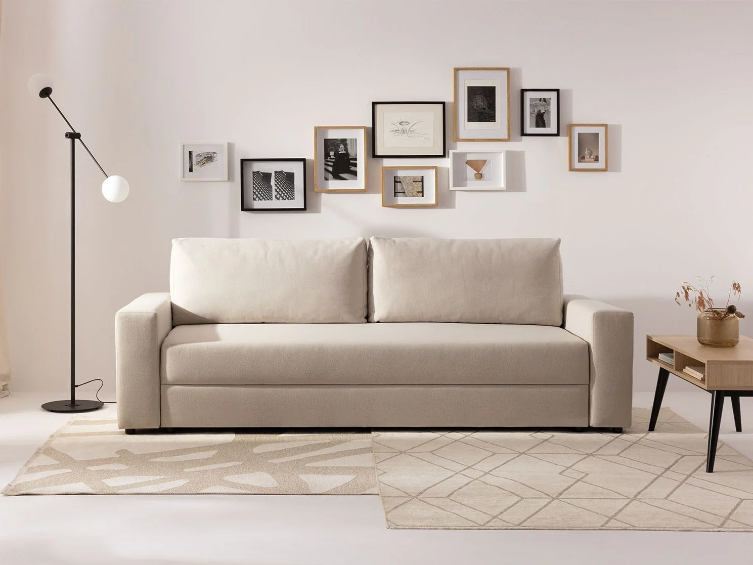 Minimalistyczny salon z beżową sofą i elegancką kompozycją obrazów na ścianie.